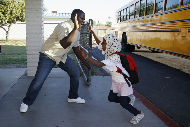 Samuel Lavi, left, a Congolese native who is a teaching assistant and family engagement liaison, greets first grader Kediga Ahmed as she arrives at the Valencia Newcomer School attend class, October 17, 2019, in Phoenix. [Photo: AP]