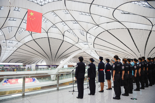 Zaměstnanci se účastní slavnostního vztyčení vlajky, které pořádá Čínská správa civilního letectví u příležitosti prvního výročí mezinárodního letiště Daxing v Pekingu dne 25. září 2020. Fotografie: tisková agentura Nová Čína / Xinhua