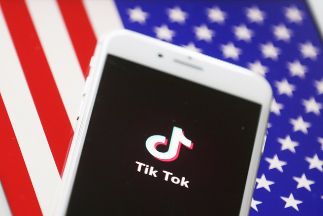 Na snímku je logo čínské sociální sítě Tik Tok pro sdílení videí zobrazené na chytrém mobilním telefonu s vlajkou Spojených států na pozadí. Fotografie: Getty