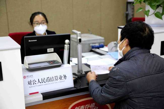 Zaměstnankyně banky pomáhá zákazníkovi se službami podnikového vypořádání v pobočce Bank of China v Lianyungang (Lien-jün-kang) v provincii Jiangsu (Ťiang-su), dne 24. února 2021. Fotografie: Wang Chun (Wang Čchun) pro deník China Daily