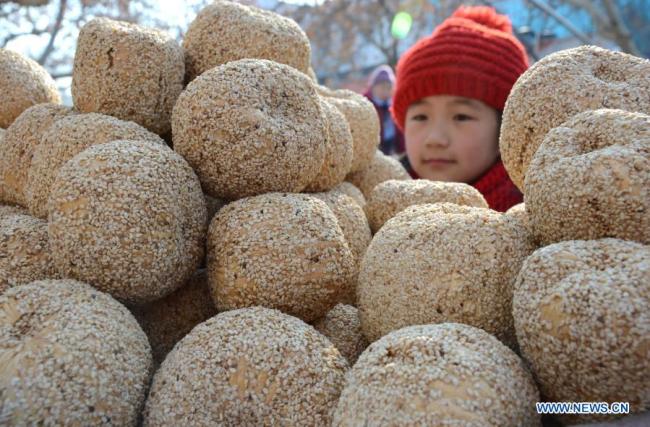 Dítě si kupuje „cukrový meloun“, lunární novoroční bonbon ze sladového cukru, lepkavé rýže a sezamu, v okrese Yiyuan (I-jüan) ve východočínské provincii Shandong (Šan-tung), 10. února 2015. Lunární Nový rok patří k nejvýznamnějším svátkům v Číně a oslavné činnosti jsou rozmanité, včetně jídla. Když přichází lunární Nový rok, lidé po celé Číně připravují různá občerstvení, která, jak věří, jim přinesou štěstí. (Foto: Zhao Dongshan / Xinhua)