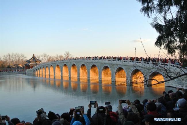Des visiteurs admirent le paysage du Pont aux Dix-Sept Arches au Palais d'Été au moment du coucher du soleil, à Beijing, capitale de la Chine, le 6 décembre 2017. (Xinhua/Ma Zhihong)
