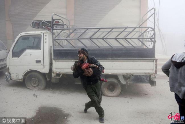 La région de la Ghouta (est de la Syrie) a été la cible le 6 février d’un raid lancé par les armées du gouvernement syrien, dont le bilan humain a été compté à une soixantaine de morts. Photo prise montrant un homme en train de fuir les lieux d’une explosion tenant dans ses bras un enfant blessé.