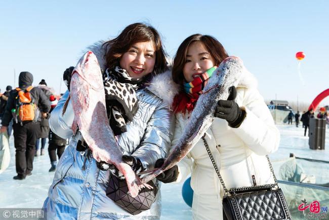 Des visiteuses posent en tenant des poissons récemment pêchés. 