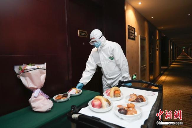 Un employé de l’hôtel en combinaison de protection distribue des fruits et des fleurs aux personnes confinées dans l’hôtel, le 24 mars, à Beijing.