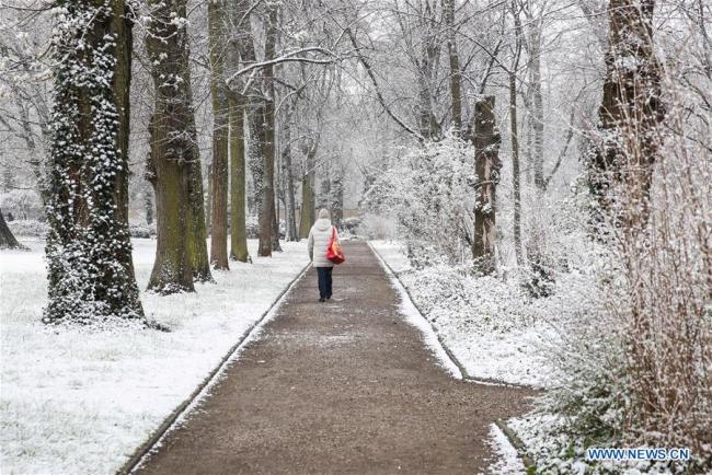 Une femme marche dans un parc après une chute de neige à Berlin, en Allemagne, le 30 mars 2020. (Xinhua/Shan Yuqi)