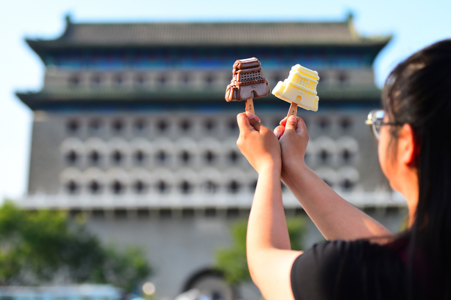Un touriste tient le sorbet en forme du Tour de Qianmen avec l'édifice comme arrière-plan (Photo crédit: VCG)