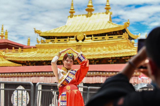 Μια τουρίστρια ποζάρει μπροστά από τον ναό Τζοκχάνγκ στη Λάσα, πρωτεύουσα της Αυτόνομης Περιοχής του Θιβέτ στις 2 Ιουλίου. [Φωτογραφία / Xinhua]