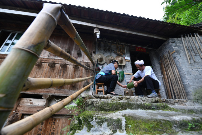 Ο χωρικός Χουάνγκ Ανχέ και η σύζυγός του φτιάχνουν χειροτεχνήματα στην είσοδο του σπιτιού τους στις 26 Ιουλίου. (Φωτογραφία / XINHUA)