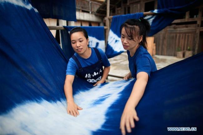 Δύο γυναίκες ισιώνουν ένα κομμάτι υφάσματος σε ένα εργαστήρι στο χωριό Φενγκντένγκ Ντονγκ της κομητείας Ρονγκτζιάνγκ, στην επαρχία Γκουιτζόου της νοτιοδυτικής Κίνας στις 6 Σεπτεμβρίου 2020. Οι Ντονγκ αυτήν την περίοδο εκμεταλλεύονται τον ωραίο φθινοπωρινό καιρό για να φτιάξουν υφάσματα με τον παραδοσιακό τρόπο ύφανσης.<br>