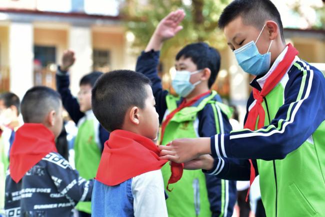 Ένας μαθητής βοηθά ένα μικρότερο συμμαθητή του με το κόκκινο μαντήλι, ως σύμβολο ότι είναι πια μέλος των Νέων Πρωτοπόρων της Κίνας στο Δημοτικό Σχολείο Γιουχουαλού στο Σιτζιατζουάνγκ, στην επαρχία Χεμπέι της βόρειας Κίνας, 12 Οκτωβρίου 2020. <br>