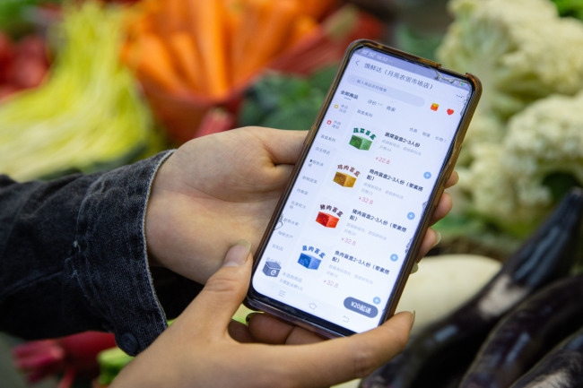 Ο Γουάνγκ Σιαογιού δείχνει σε κινητό τηλέφωνο τη λίστα με τα πιάτα μυστηρίου που προσφέρει στο διαδίκτυο σε μια αγορά στην Ναντζίνγκ, στην επαρχία Τζιανγκσού, την 1η Νοεμβρίου 2020. [Φωτογραφία: CNSPHOTO]