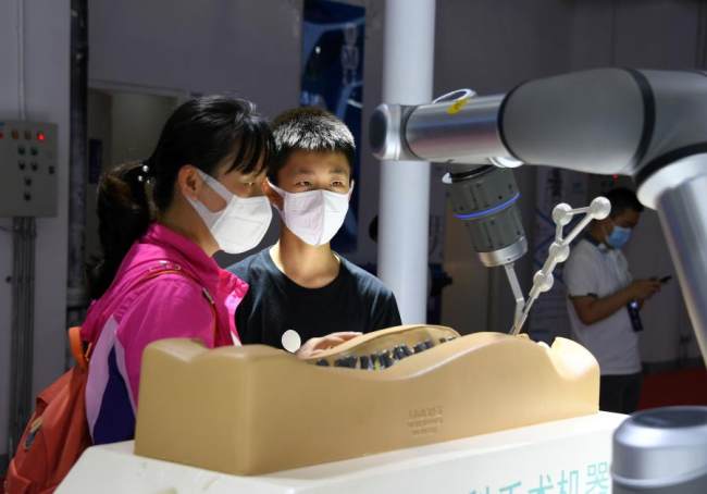 Návštěvníci na výstavě pekingské World Robot Expo sledují robota při ortopedické operaci, 12. září 2021. [Photo/Xinhua]