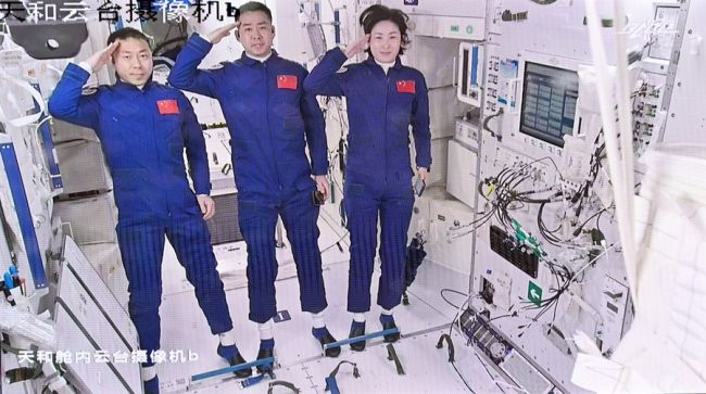 Snímek obrazovky z pekingské Centra aerokosmického řízení 5. června 2022 ukazuje tři taikonauty Chen Dong (střed), Liu Yang (vpravo) a Cai Xuzhe salutující po přestoupení do základního modulu stanice Tianhe. (Xinhua/Xinhua)