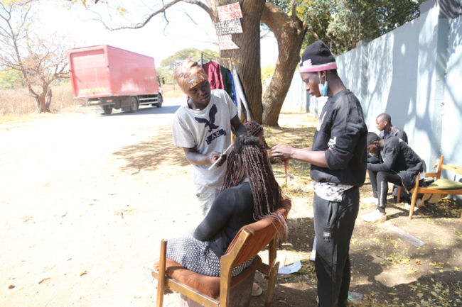 Lovemore Gavaza kaj lia pli juna frato Learnmore Gavaza mastrumas subĉielan “frizosalonon” sub siringa arbo en zono Avondale de la zimbabva ĉefurbo Hararo.
