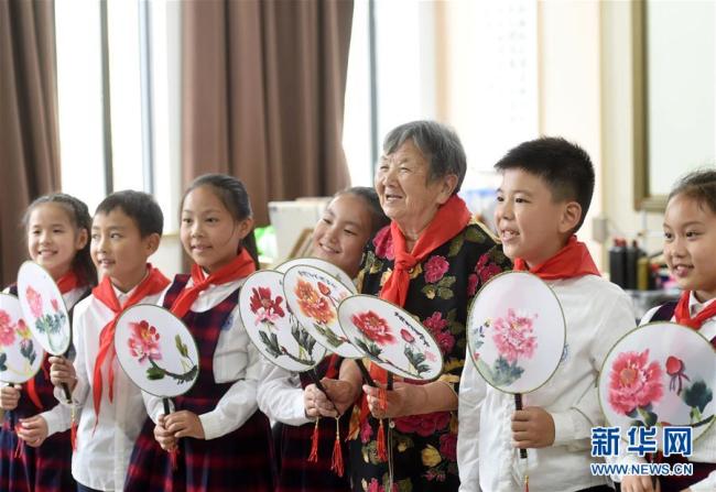 Ying Miaofang und Grundschüler zeigen die von ihnen gemachten mondförmigen Fächer. 
