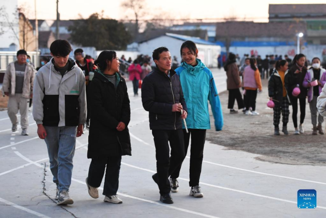 Ο Λου Γουεντζιάν (2ος δεξιά) περπατά με μαθητές στο σχολείο στο Σανγκτσιό, στην επαρχία Χενάν της κεντρικής Κίνας, 2 Δεκεμβρίου 2021. (Xinhua/Zhang Haoran)