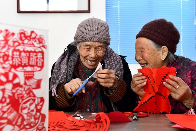 Δύο ηλικιωμένες γυναίκες συνομιλούν ενώ ασχολούνται με παραδοσιακή χαρτοκοπτική σε ένα κέντρο φροντίδας ηλικιωμένων στο χωριό Χουανγκτζιαγιού του Ριτζάο, στην επαρχία Σανντόνγκ της Ανατολικής Κίνας, σε φωτογραφία από τις 27 Φεβρουαρίου 2022. [Φωτογραφία/Xinhua]